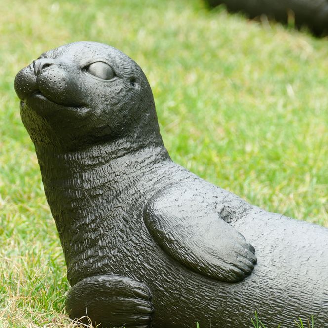 Bronzene Seehundfigur liegt auf einer Wiese