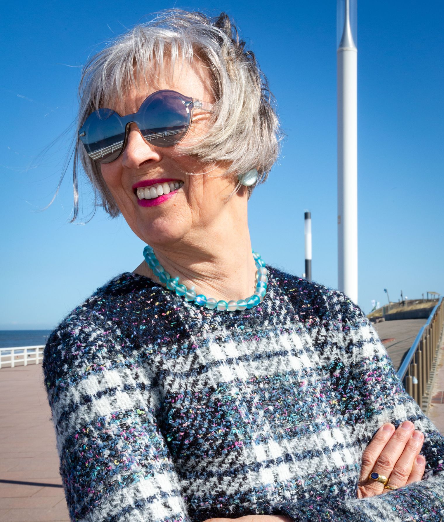 Frau mit Sonnenbrille steht lächelnd an einer Promenade auf Sylt.