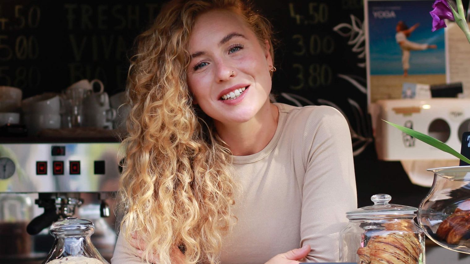 Junge Frau mit Locken lächelt hinter Cafétheke