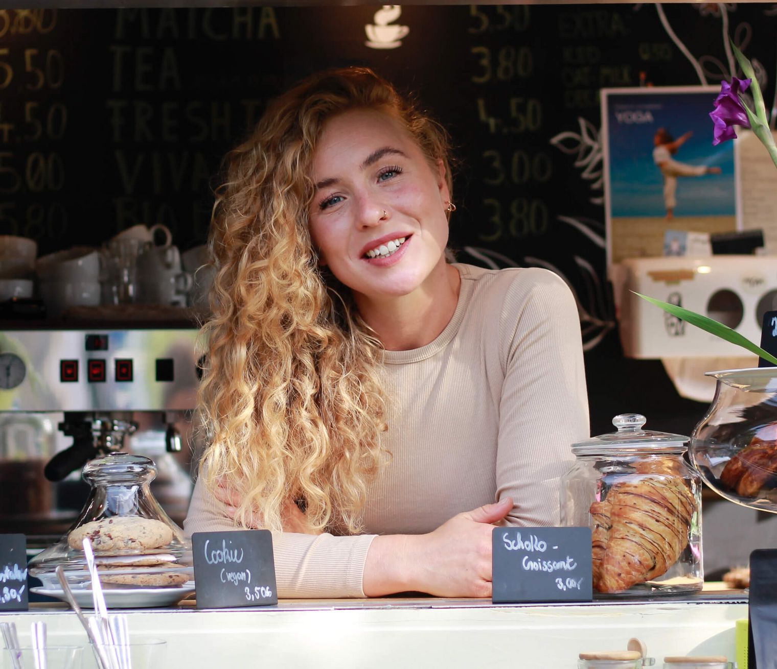Junge Frau mit Locken lächelt hinter Cafétheke