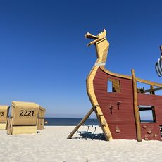 Wikingerschiff-Klettergerüst und Strandkörbe auf Sandstrand vor blauem Himmel und Meer.