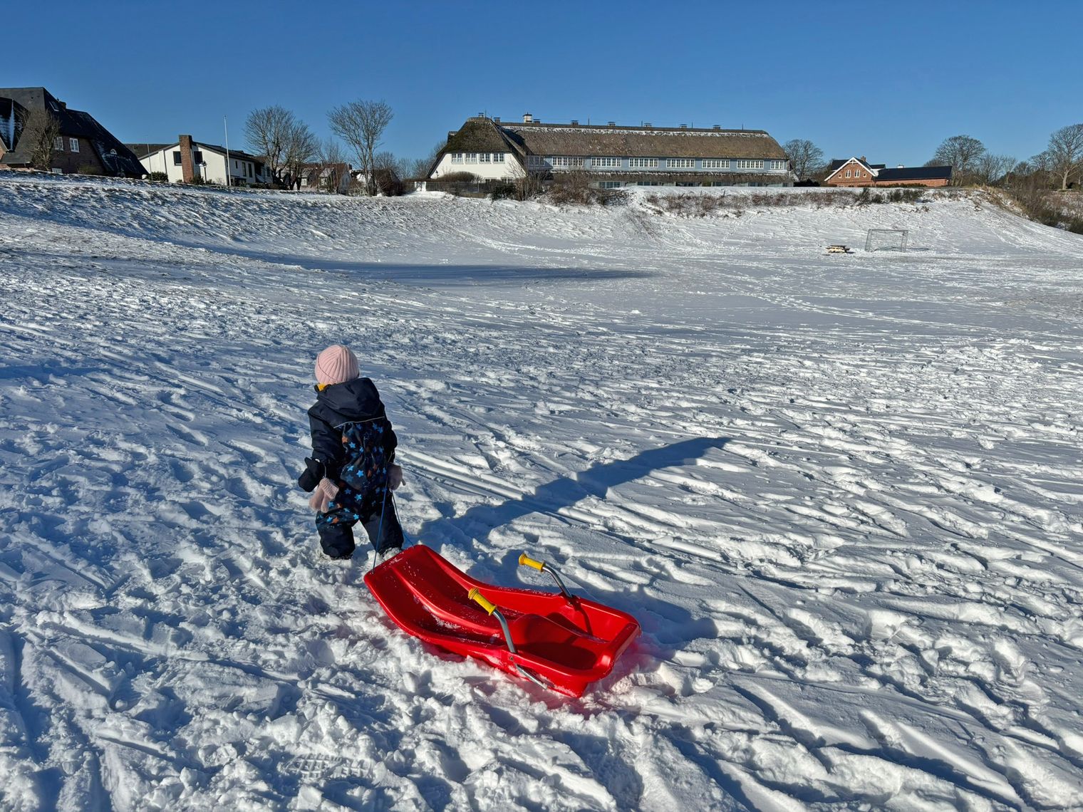 Mädchen im Schneeanzug zieht roten Plastikschlitten durch den Schnee