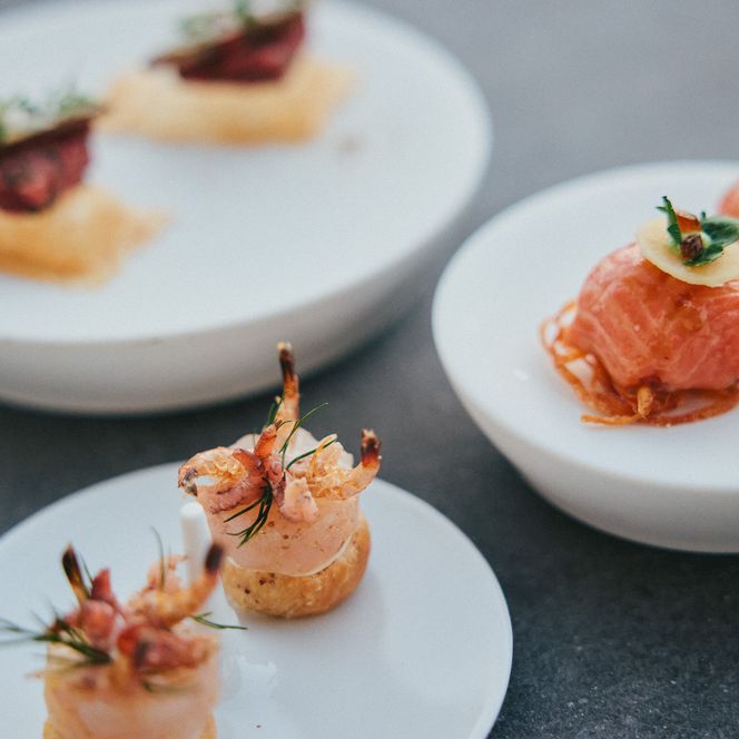 Häppchen aus Meeresfrüchten, Lachs und knusprigen Toppings auf weißen Tellern.