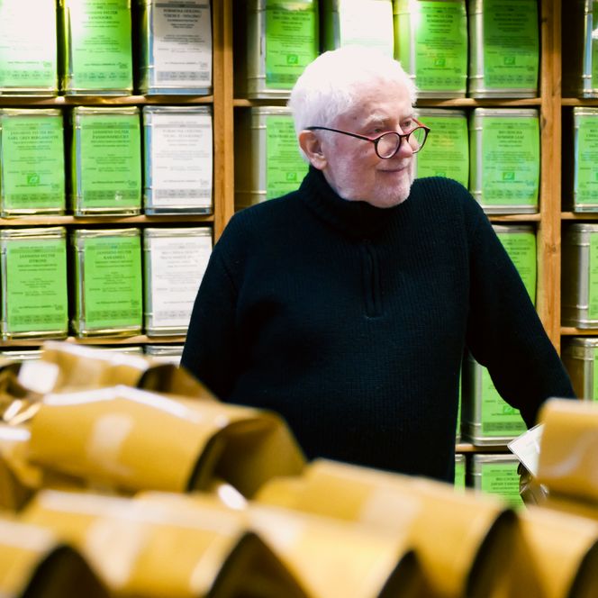 Älterer Mann steht vor Regal mit grünen Teedosen