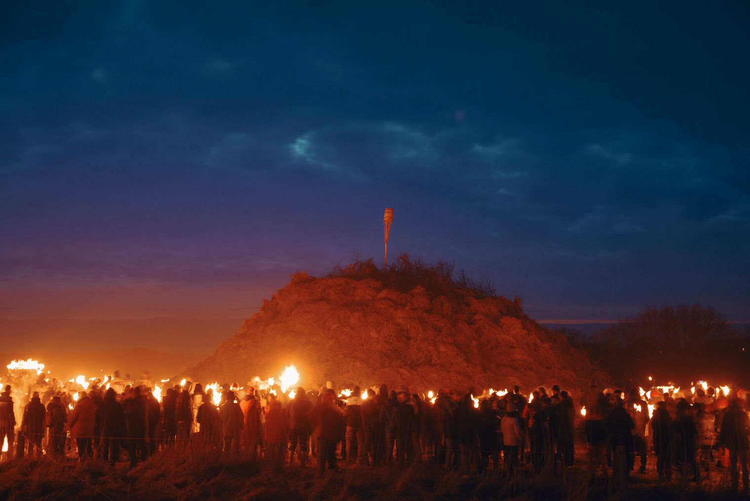 Menschen mit Fackeln vor großem Biikehaufen in Westerland bei Dämmerung
