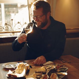 Mann genießt Weißwein und Austern bei Sonnenlicht