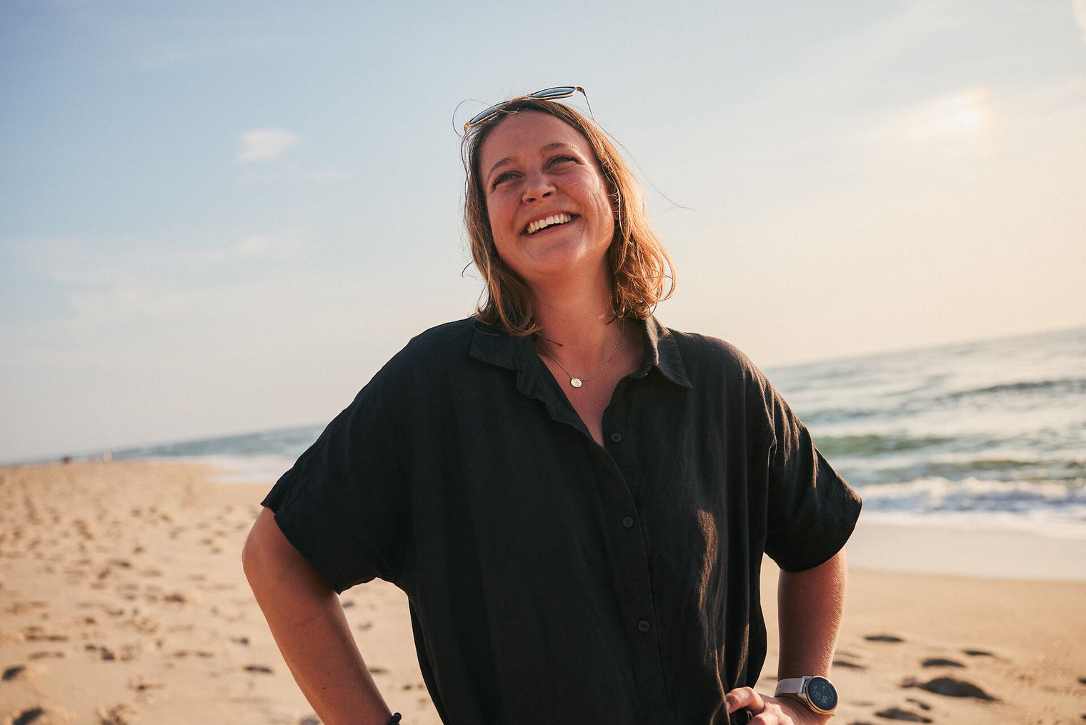 Eine Frau in schwarzem Shirt steht lachend am Strand.