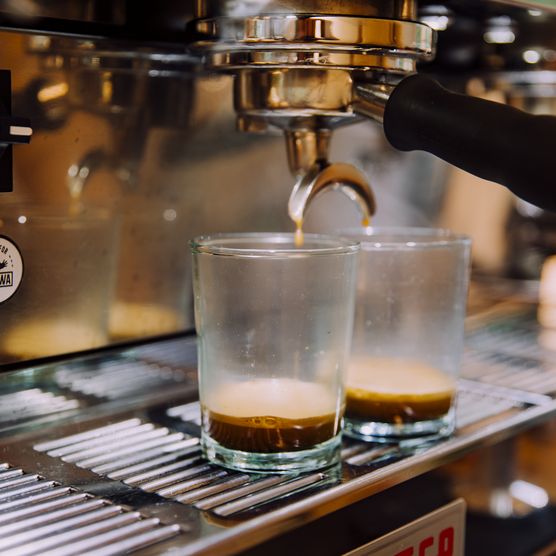 Espressomaschine brüht zwei Espressoshots in klaren Gläsern auf Metallgitter.