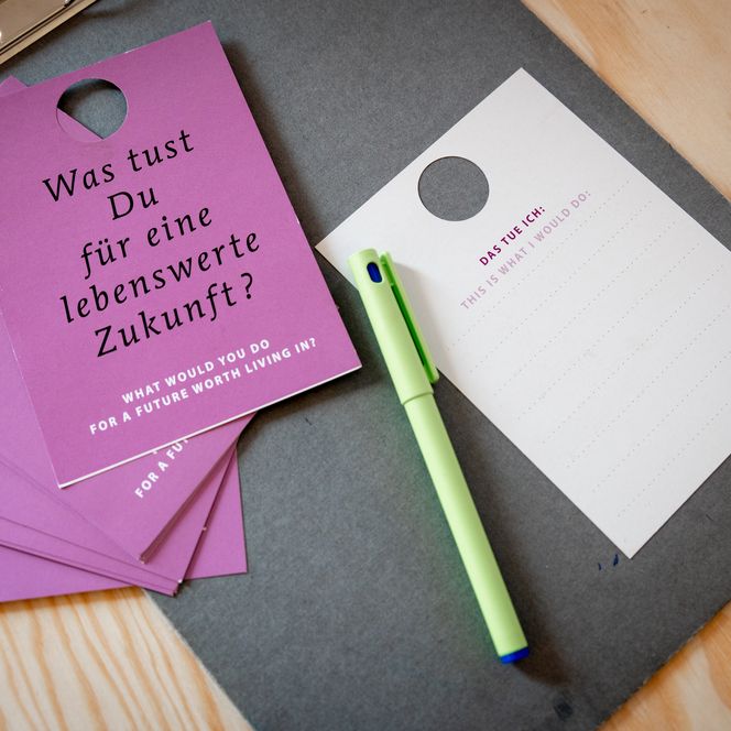 Zettel mit der Aufschrift "Was tust du für eine lebenswerte Zukunft" liegen auf einem Tisch, daneben ein Stift.