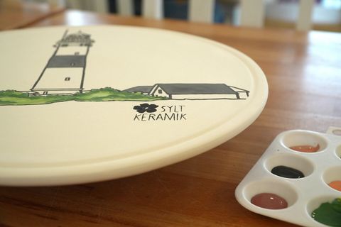 Keramikteller mit Leuchtturmmotiv und Aufschrift „Sylt Keramik“, daneben eine Farbpalette mit mehreren Farbtupfern.