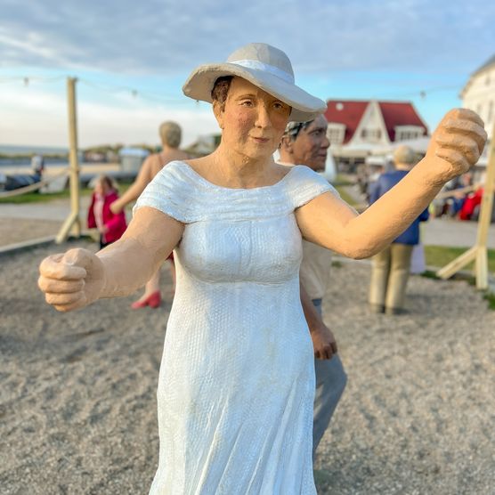 Eine weibliche Figur im schwingenden weißen Kleid und Hut tanzt
