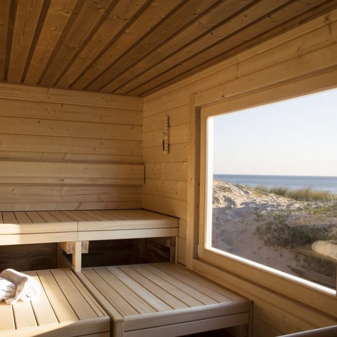 Helle Holzsauna mit Sitzbänken und großem Fenster zum Meer.
