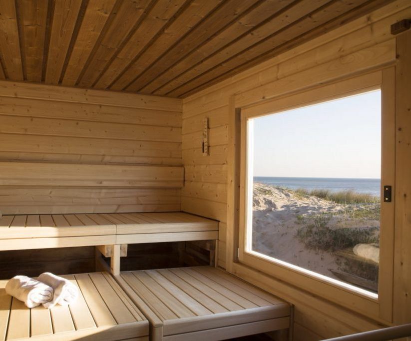 Helle Holzsauna mit Sitzbänken und großem Fenster zum Meer.