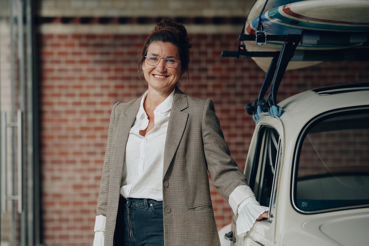 Anne Stahl von Sylt Marketing steht lächelnd neben einem Fahrzeug mit Surfbrett auf dem Dach.