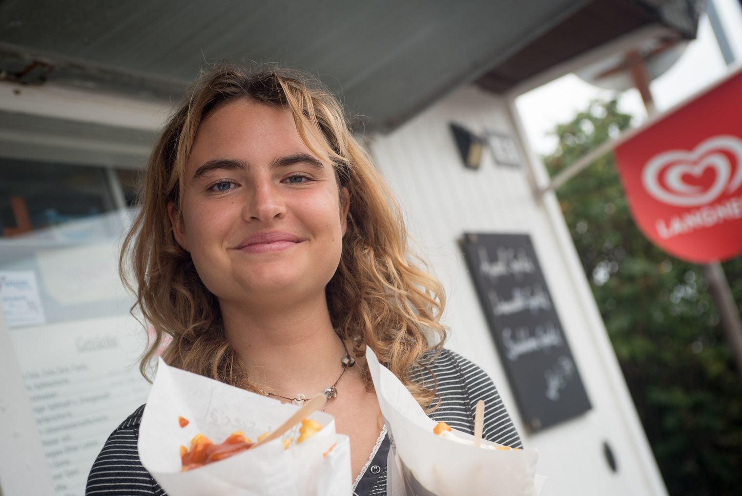 Junge Frau hält zwei Portionen Pommes vor der Zauberbude auf Sylt.