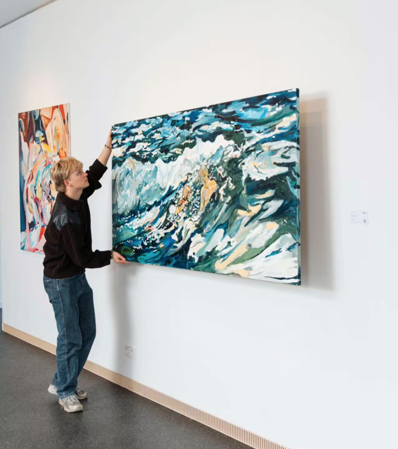 Person hängt großes abstraktes Gemälde an weißer Wand auf