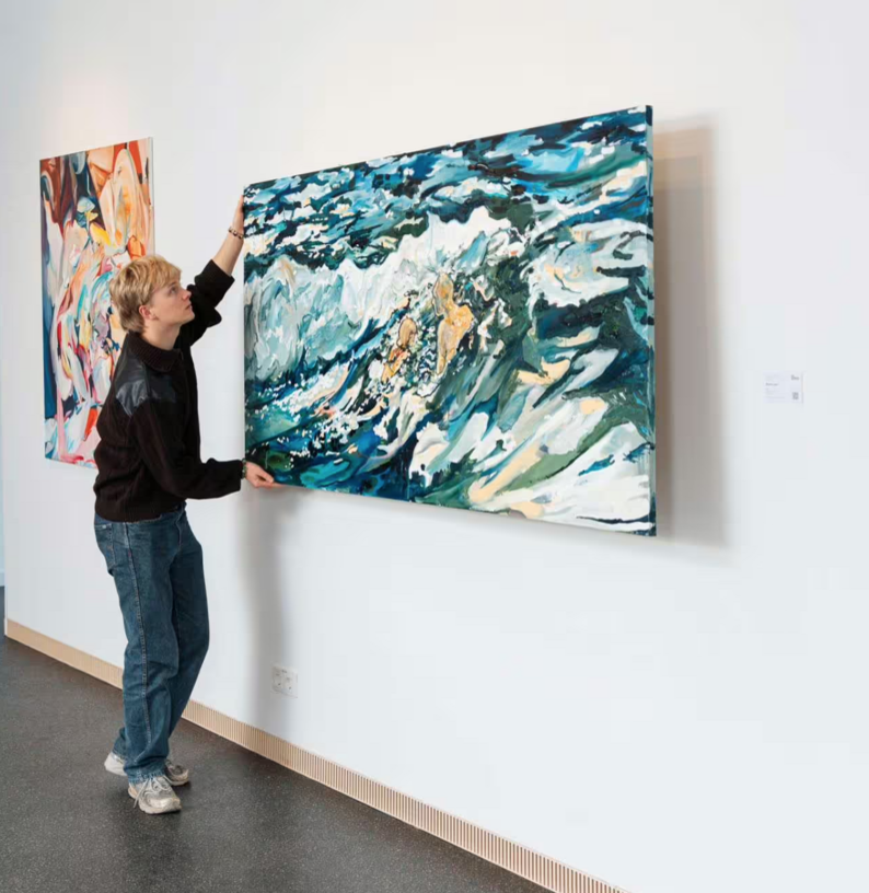 Person hängt großes abstraktes Gemälde an weißer Wand auf