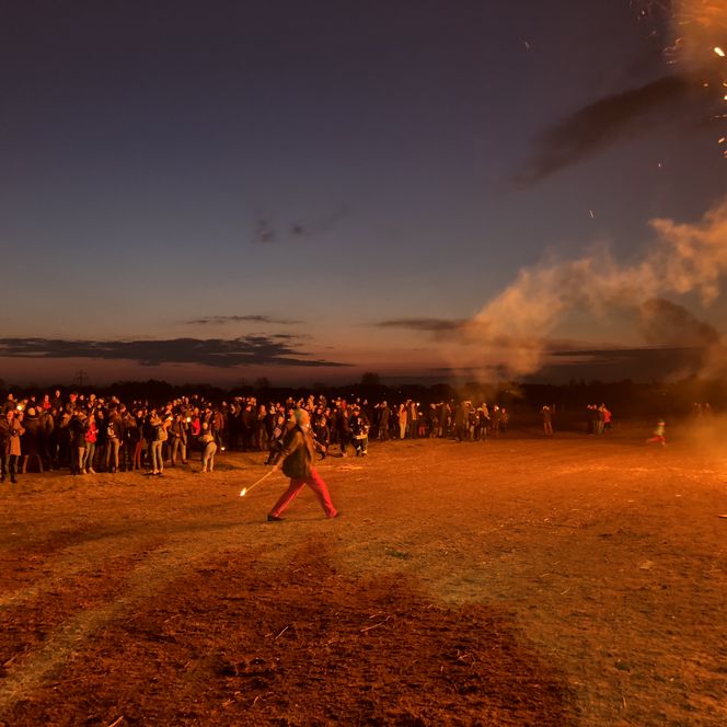 Menschen werfen Fackeln in ein großes Feuer beim Biikebrennen in der Dämmerung.