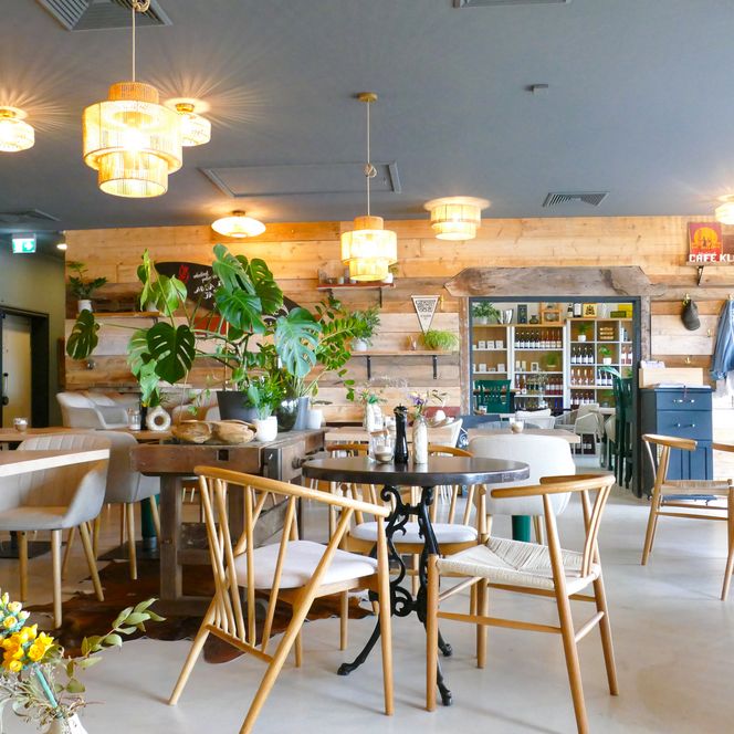 Café-Innenraum mit Holzmöbeln, Pflanzen und Regalen im Hintergrund