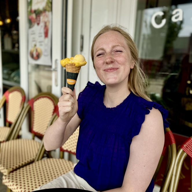 Du sitzt vor einem Café und hältst eine Eiswaffel mit zwei Kugeln Eis in der Hand.
