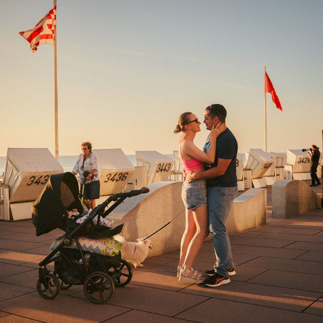 Paar umarmt sich an Promenade im Abendlicht mit Kinderwagen.
