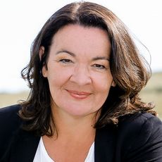 Porträt einer Frau mit mittellangem braunem Haar, die freundlich in die Kamera lächelt.