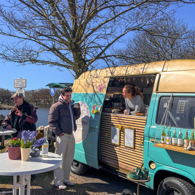 ein restaurierter VW T3 Bus steht vor dem Dorfteich. Einige Personen stehen an stehtischen davor.