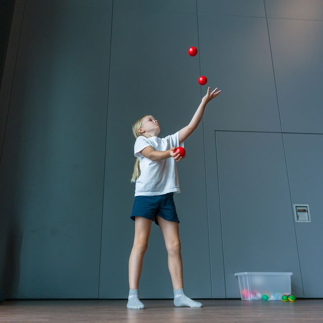 Kind jongliert mit roten Bällen in Turnhalle