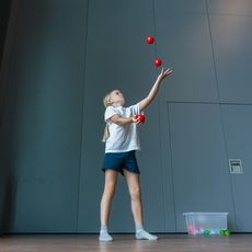 Kind jongliert mit roten Bällen in Turnhalle