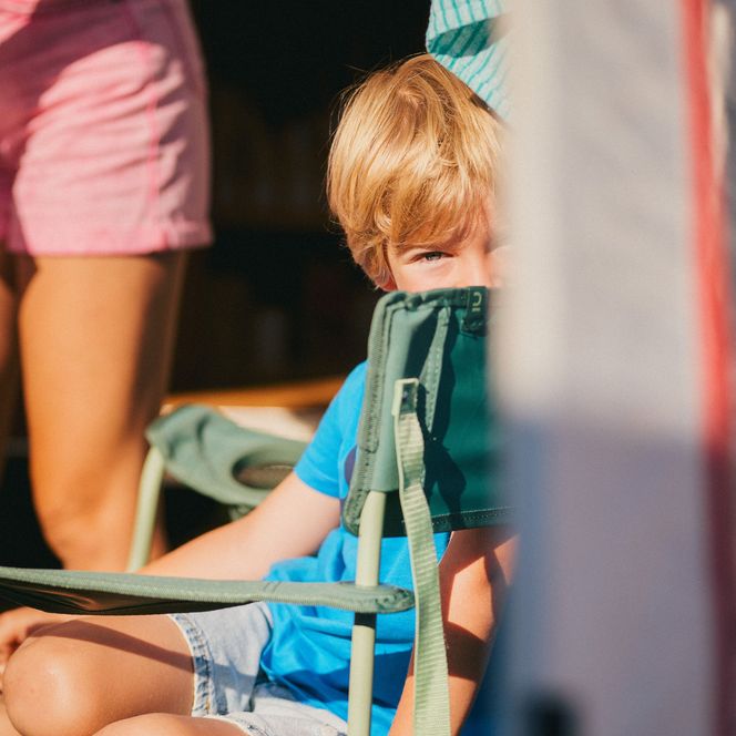 Ein Junge schaut neugierig hervor, während er auf einem Campingstuhl sitzt.