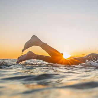 Surferbeine ragen aus dem Wasser, Sonnenuntergang leuchtet durch die Wellen.