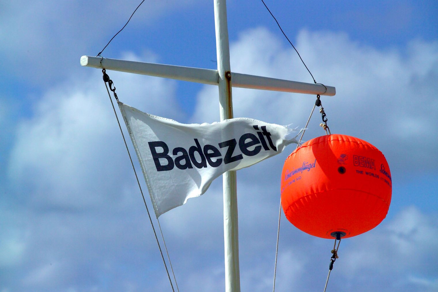 Fahne mit Aufschrift „Badezeit“ weht neben orangener Boje