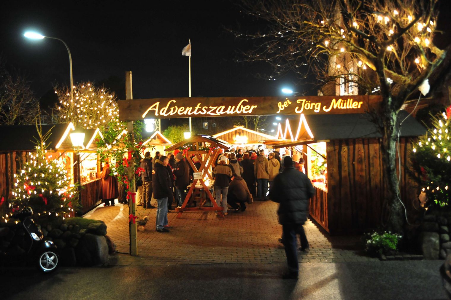 Adventszauber bei Jörg Müller: Beleuchteter Weihnachtsmarkt mit geschmückten Bäumen und festlicher Atmosphäre bei Nacht.