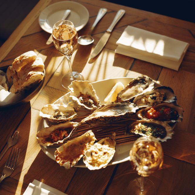 Teller mit Austern, zwei Gläser Champagner und Brot im Sonnenlicht