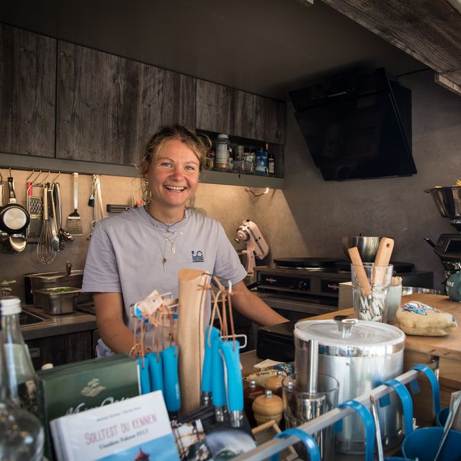 Junge Frau lächelt in Foodtruck-Küche mit Küchenutensilien.