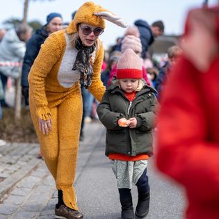 Kind balanciert Ei beim Ostereierlauf, begleitet von Frau im Hasenkostüm