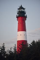 Der Hörnumer Leuchtturm auf Sylt, rot-weiß gestreift, mit blauem Himmel im Hintergrund.