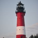 Der Hörnumer Leuchtturm auf Sylt, rot-weiß gestreift, mit blauem Himmel im Hintergrund.