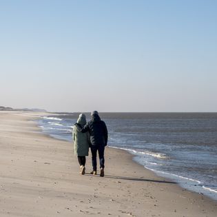 Paar in Winterkleidung spaziert am leeren Strand entlang des Meeres.
