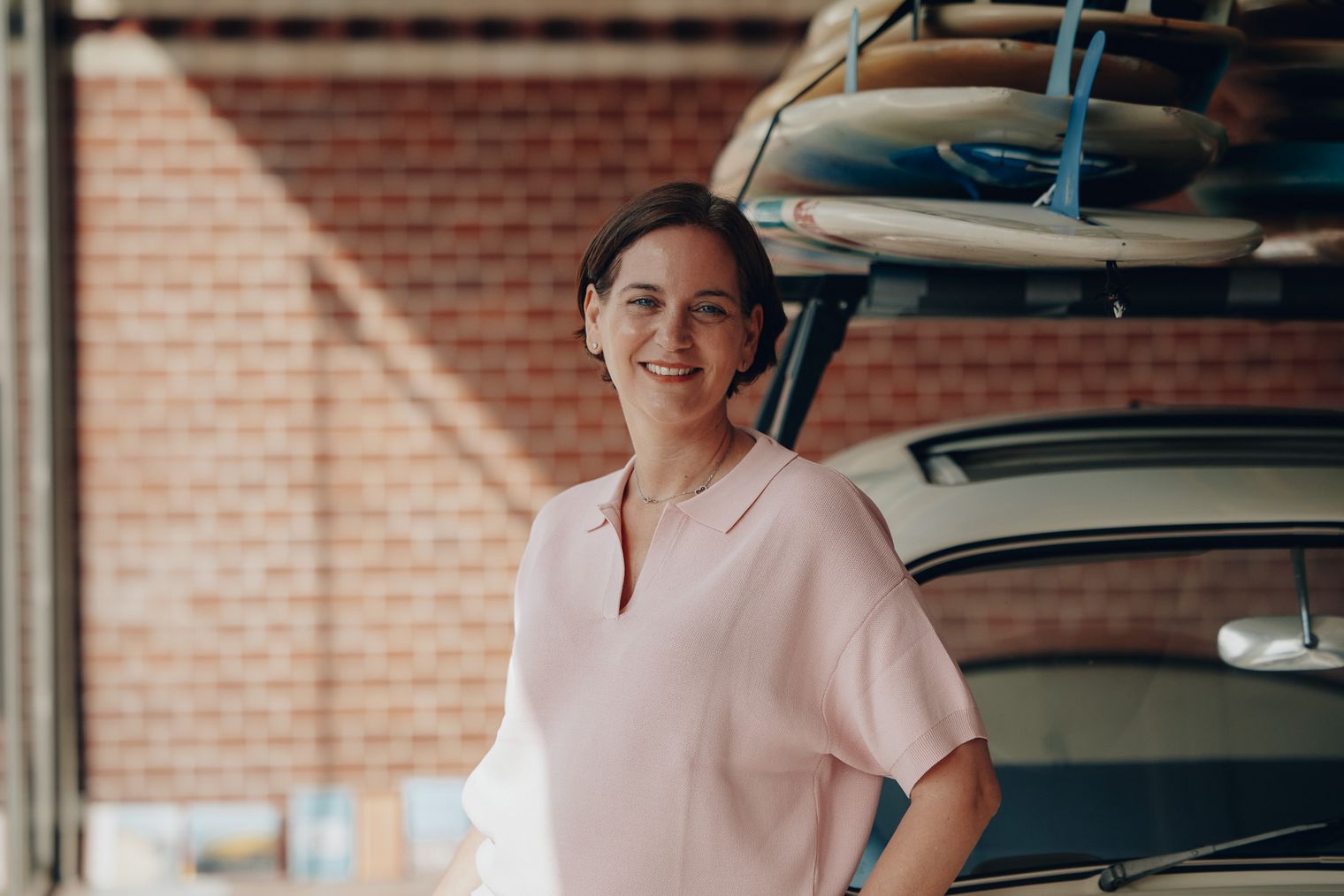 Kathrin Barz von Sylt Marketing steht vor einem Auto mit Surfboards und lächelt in die Kamera.