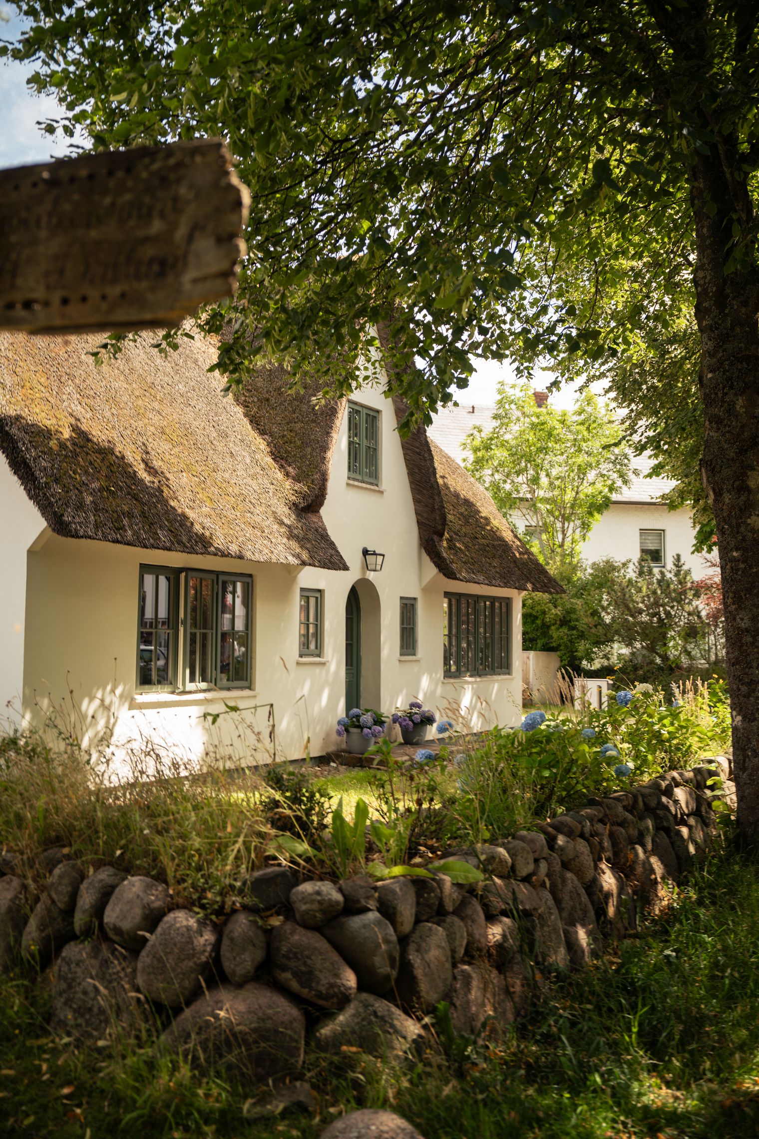 Reetdachhaus mit Garten, Steinmauer und Bäumen im Vordergrund