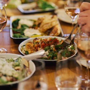 Verschiedene mediterrane Speisen und Gläser Roséwein auf einem gedeckten Tisch, eine Person nimmt eine Gabel voll Essen.