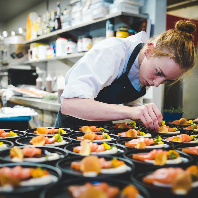 Köchin verziert Teller mit Lachs in Restaurantküche
