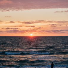 Person steht am Strand und blickt auf das Meer bei Sonnenuntergang.