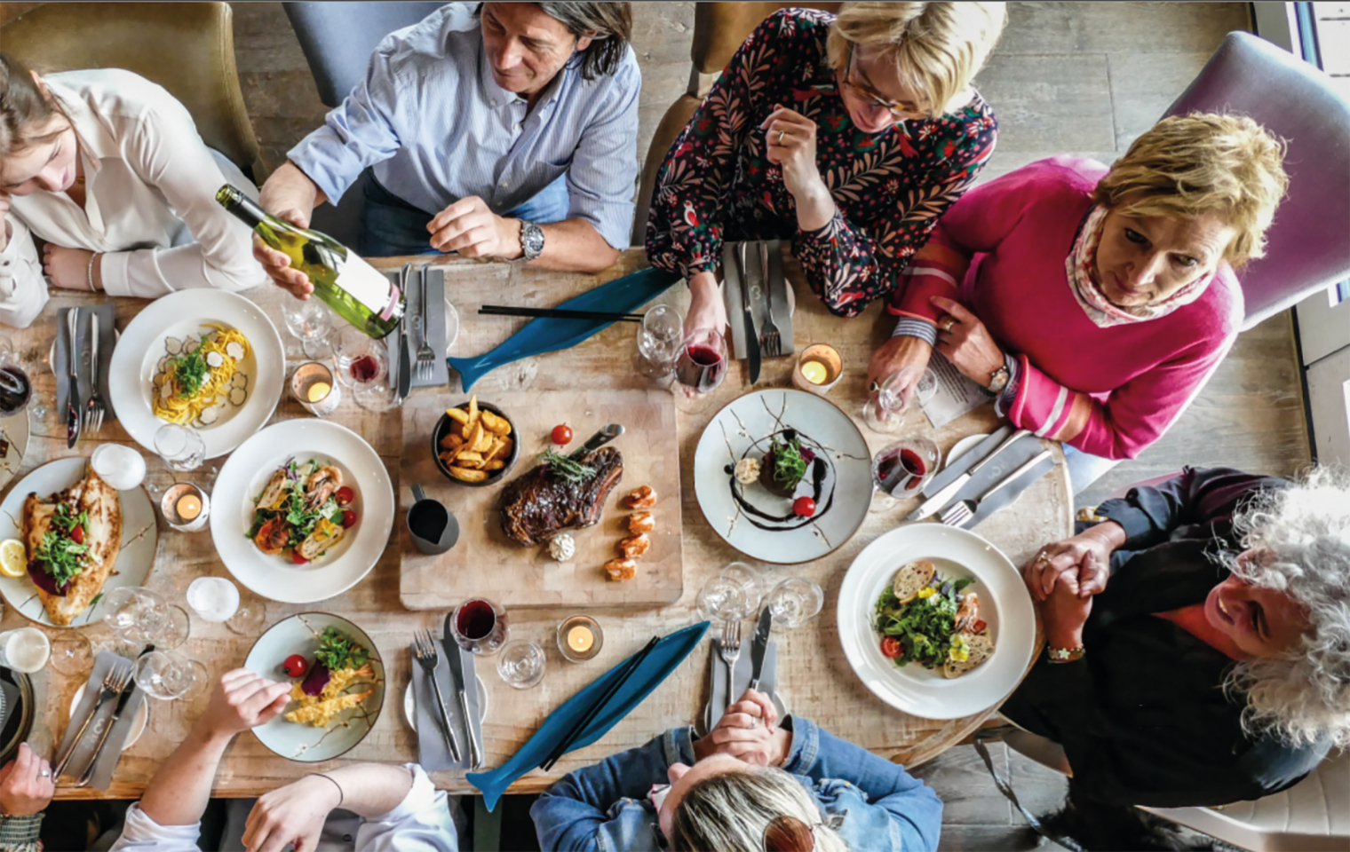 Menschen genießen gemeinsam ein Abendessen im Restaurant Coast in Rantum auf Sylt, mit Wein und verschiedenen Gerichten.