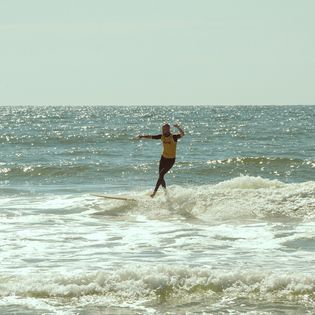 Surfer auf Longboard gleitet über eine kleine Welle.