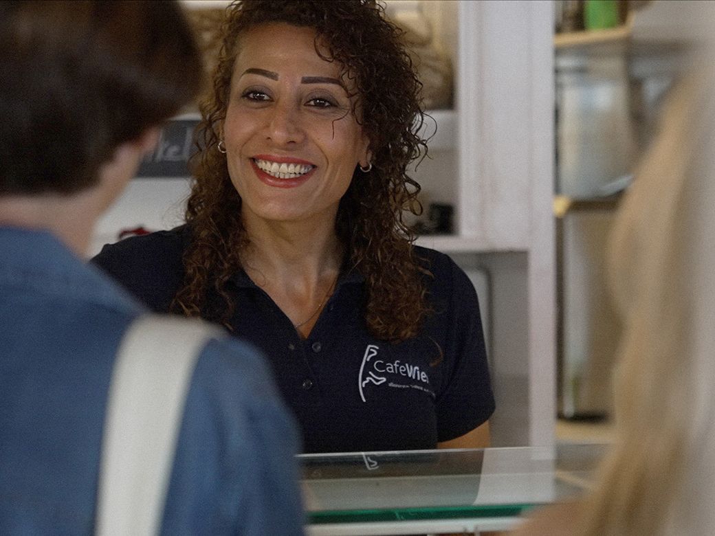 Mitarbeiterin Eman im Café Wien in Westerland begrüßt eine Kundin an der Verkaufstheke.
