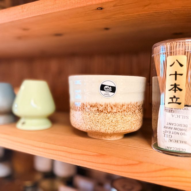 Teeschale, Keramikgefäße und Matcha-Besen auf Holzregal