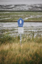 Nationalpark-Schild mit Eulen-Symbol vor dem Wattenmeer und Salzwiesen.