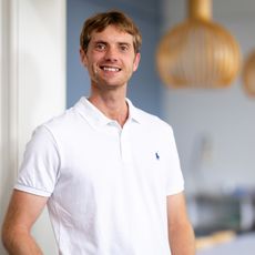 Mann in weißem Polohemd lächelt vor modernem Besprechungsraum